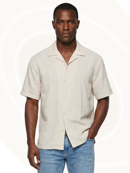 Man wearing an off white embroidered short-sleeve shirt and blue jeans on a white background