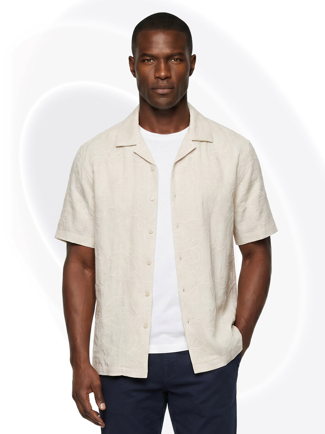 Man wearing an off white embroidered short-sleeve shirt over a white t-shirt on a white background