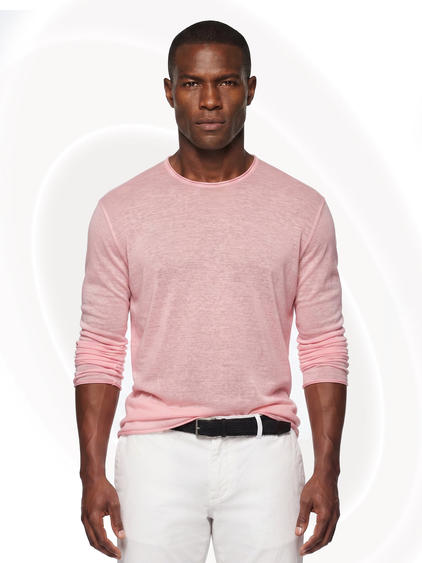 A man wearing a light pink long-sleeve crewneck shirt and white pants, standing against a white background with subtle circular patterns.