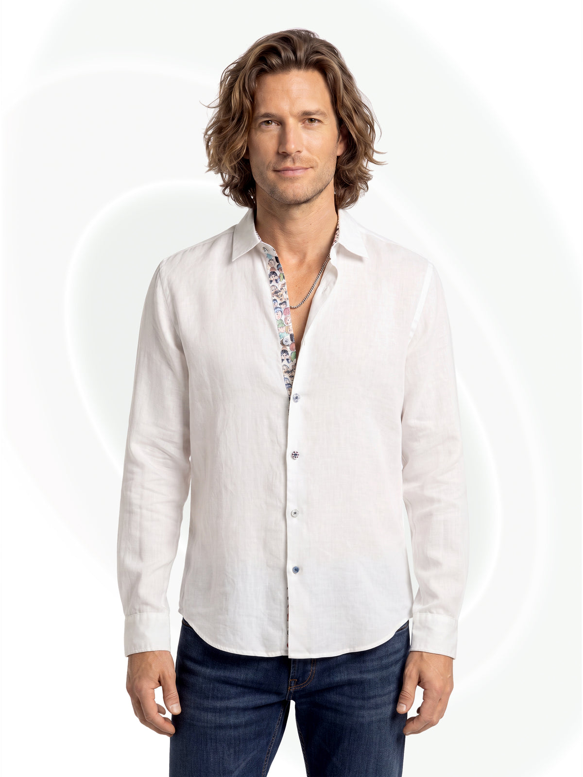 A man wearing a white long-sleeve linen button-down shirt over a patterned undershirt, paired with dark blue jeans, against a light gray background with faint circular graphic overlays.