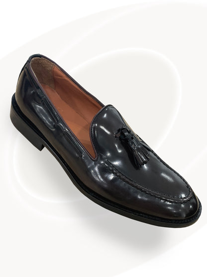 Black patent leather loafer with a tassel on a white background