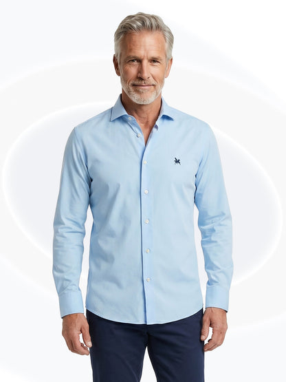 Man wearing a light blue dress shirt with a small logo on a white background
