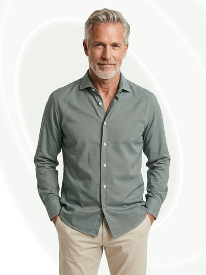 Man wearing a green button-up shirt and beige pants on a white background