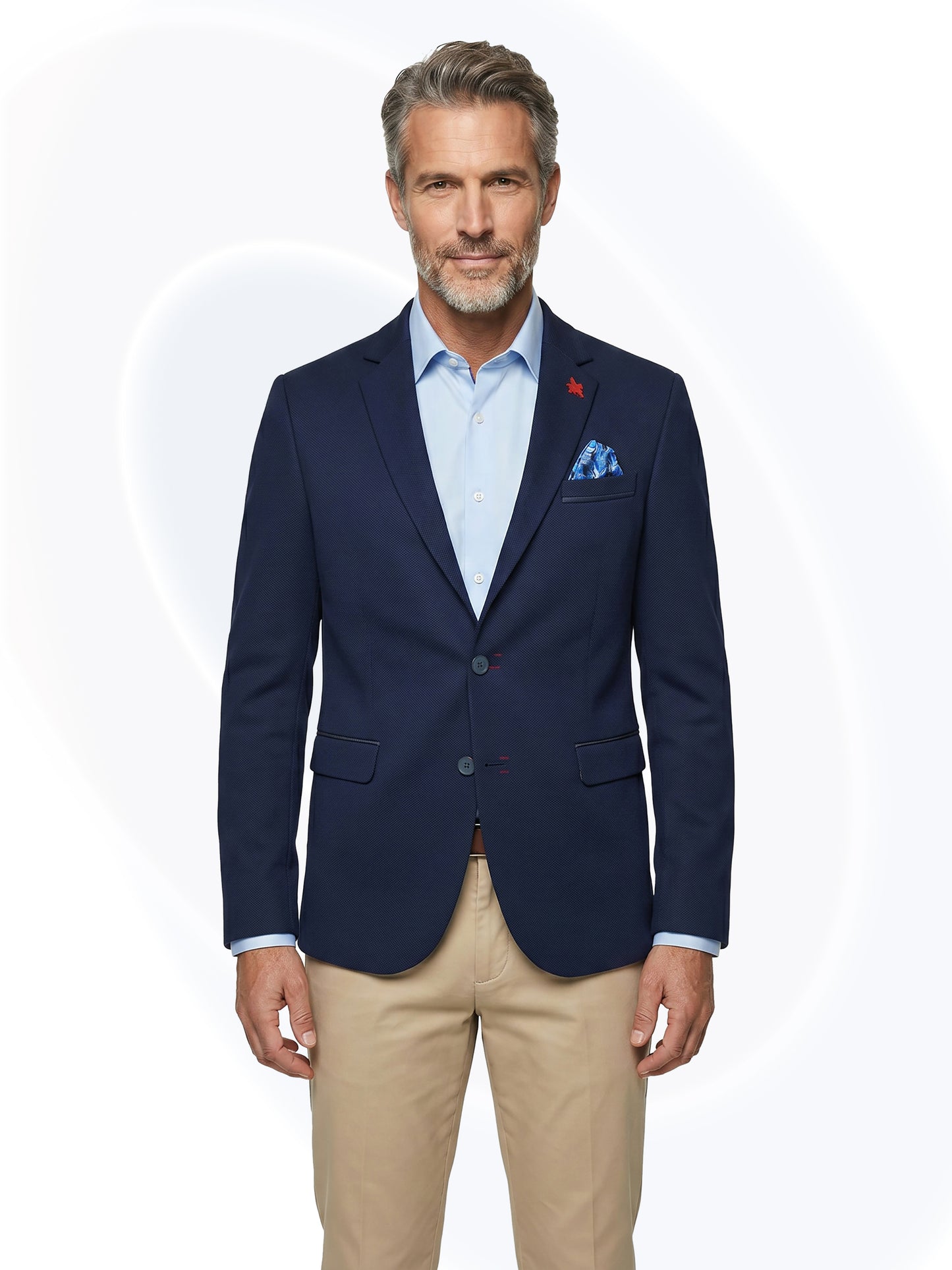 Man wearing a navy blazer with a light blue shirt and beige pants on a white background