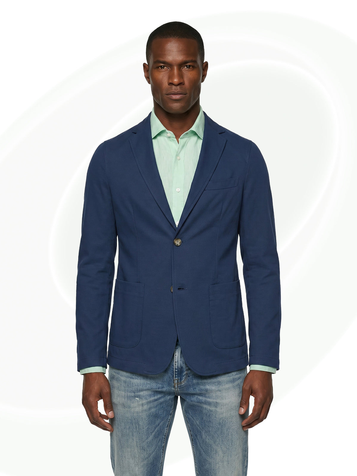 Man wearing a navy blazer over a light green shirt and jeans on a white background