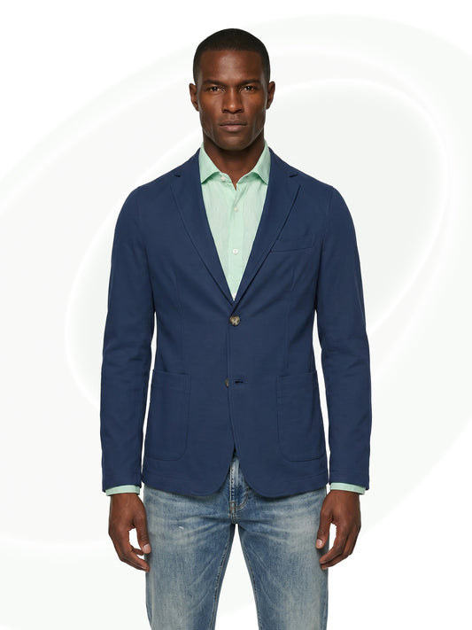 Man wearing a navy blazer over a light green shirt and jeans on a white background