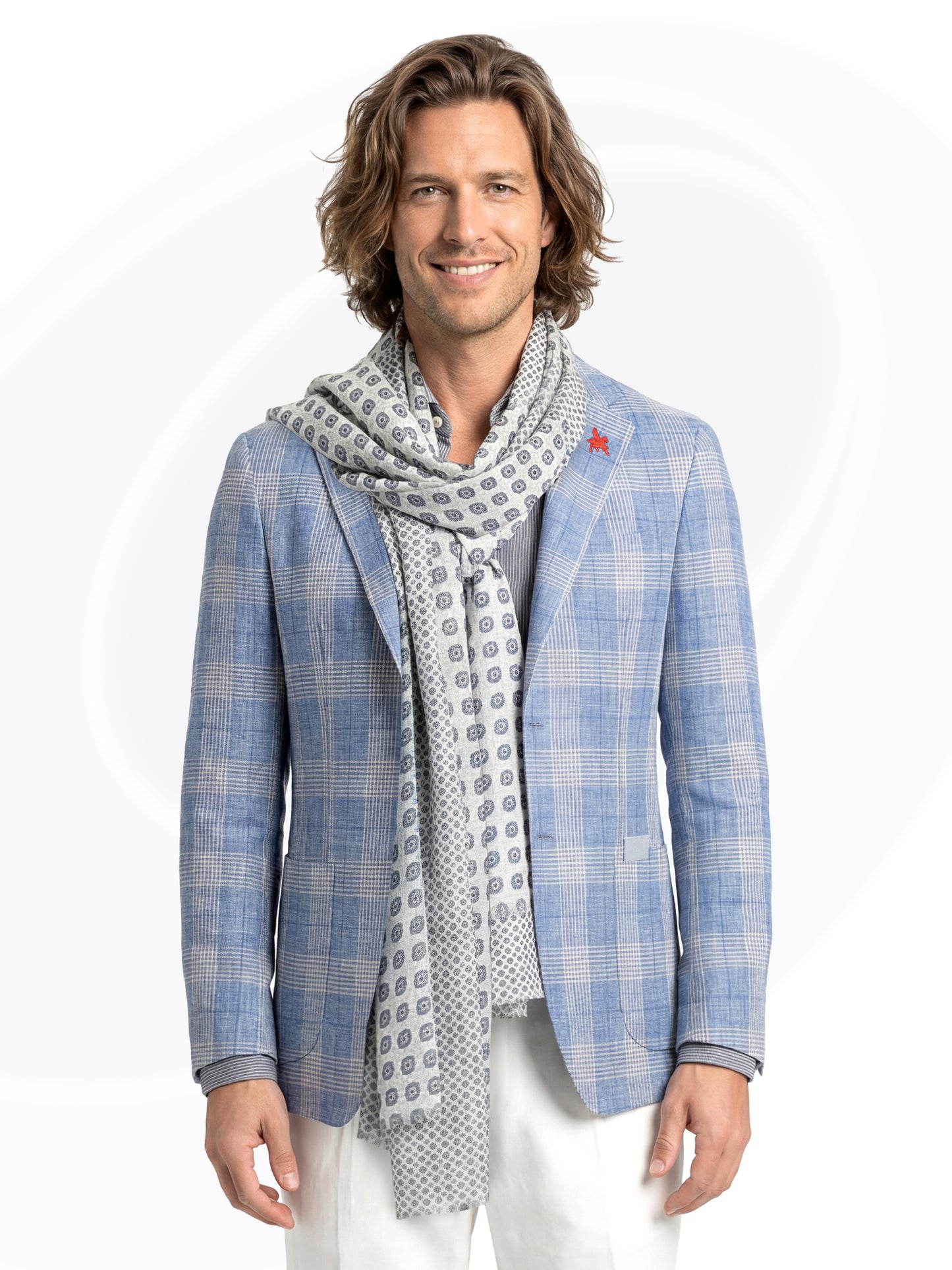 Man wearing a blue checkered blazer and patterned scarf and white pants on a white background