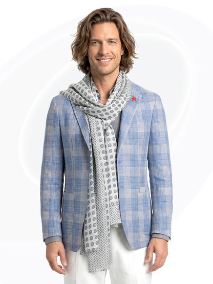 Man wearing a blue checkered blazer and patterned scarf and white pants on a white background