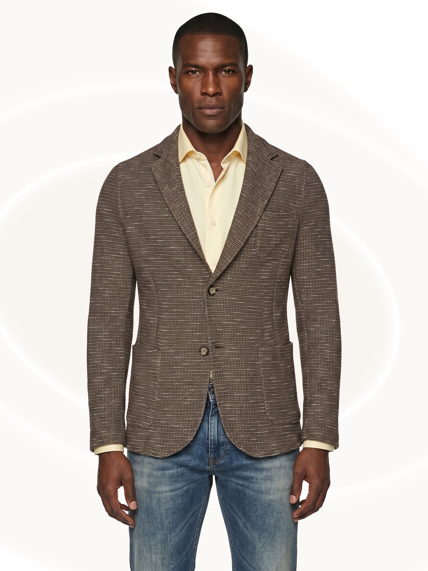 Man wearing a brown fitted blazer over a yellow shirt and blue jeans on a white background
