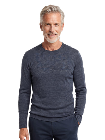 A smiling older man with gray hair and a beard wearing a dark heathered blue long-sleeve crewneck sweater and dark pants, standing against a plain white background.