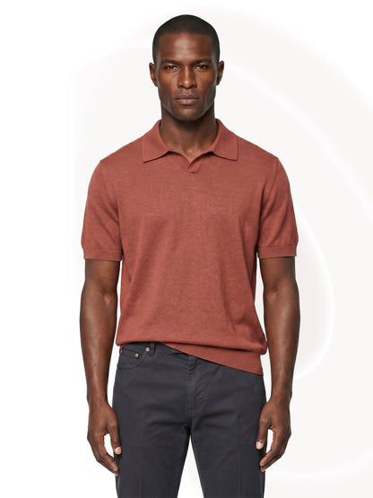 Man wearing a copper polo shirt and dark pants on a white background