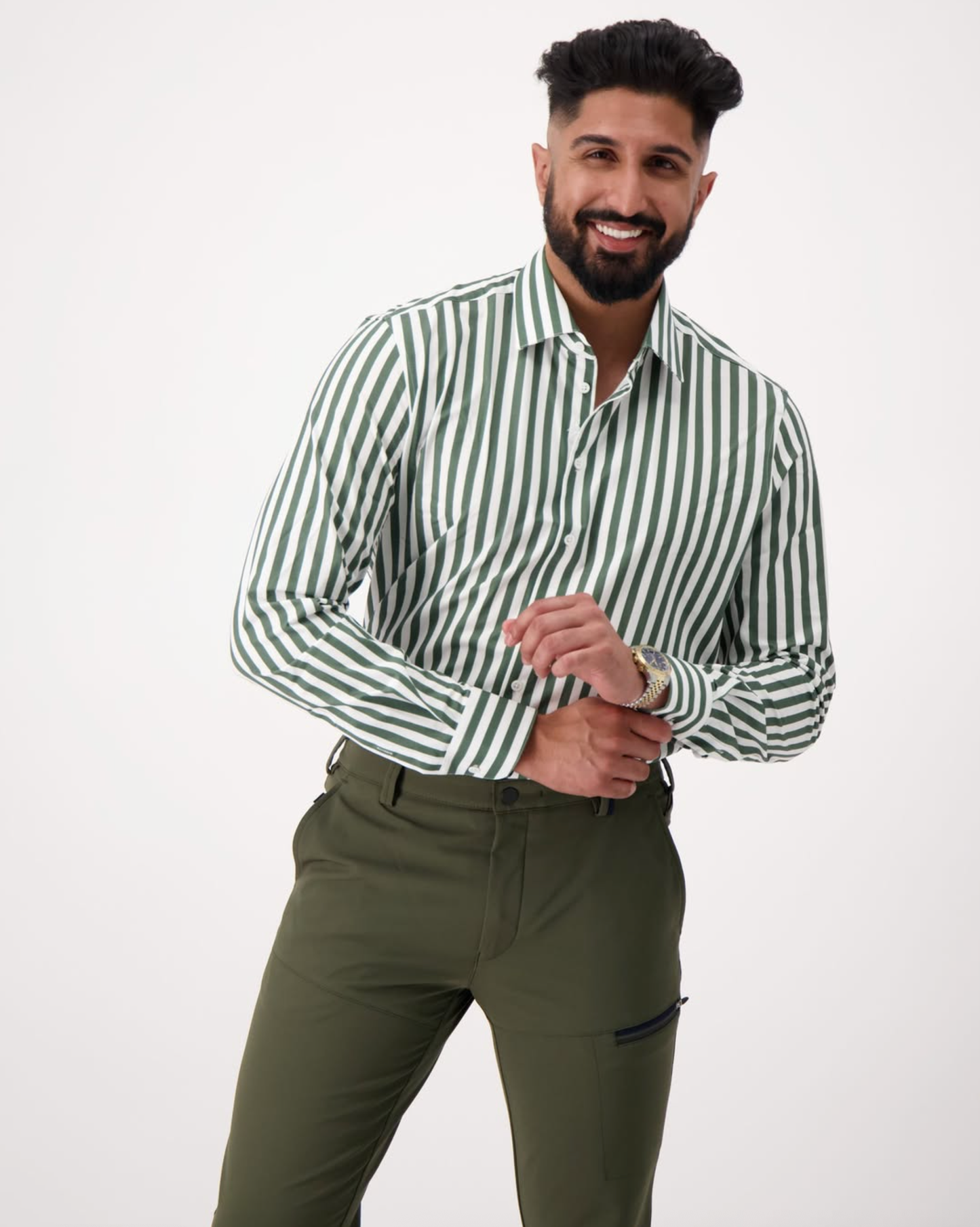 Man wearing a green and white striped Essential Shirt with rolled-up sleeves and olive trousers, smiling against a white background — Eric Sana.