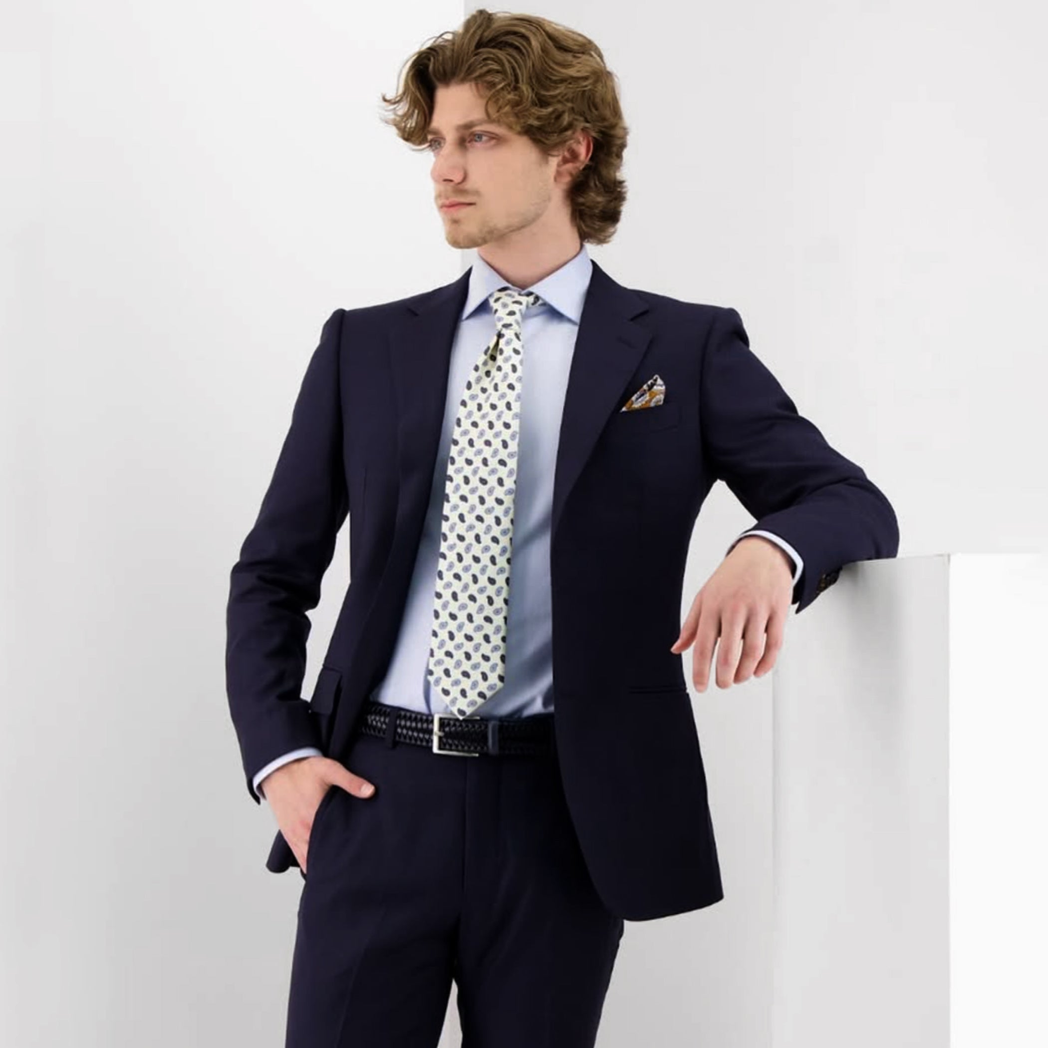 Man wearing a navy suit with a light blue shirt and patterned tie on a white background